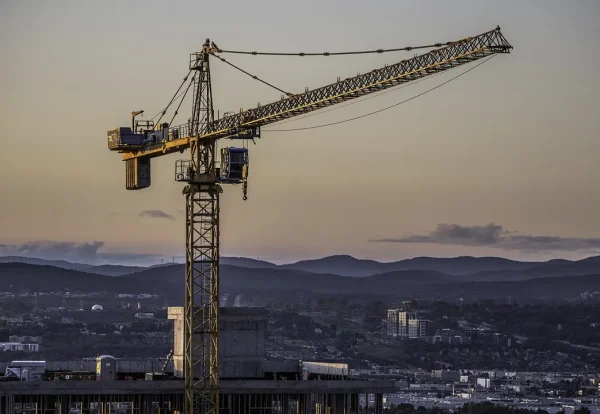 Tower crane at dusk over a city: delayed handover Dubai off-plan projects depend on construction progress