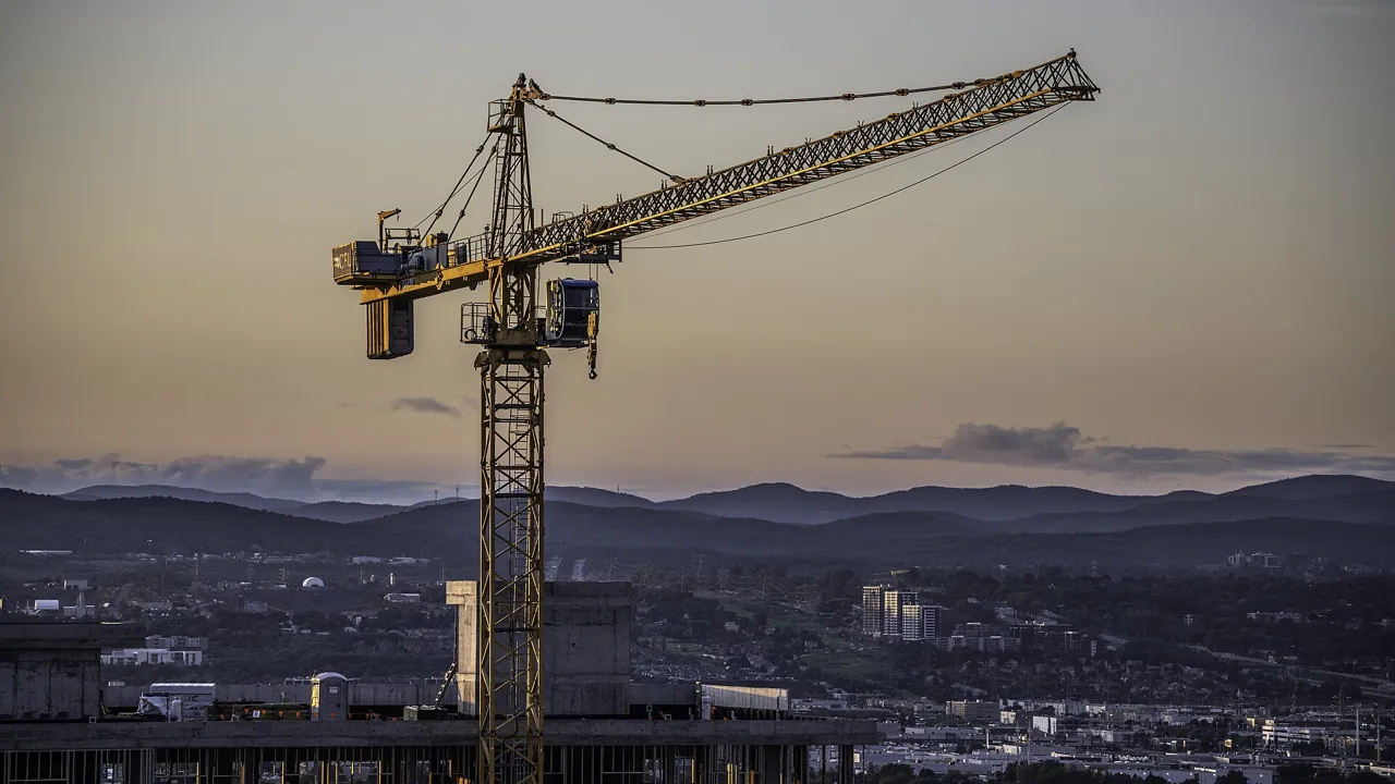Tower crane at dusk over a city: delayed handover Dubai off-plan projects depend on construction progress
